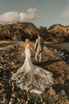 a bride and groom walking on the beach holding hands with palm trees in the background