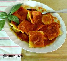 a white plate topped with ravioli covered in marinara sauce and spinach leaves