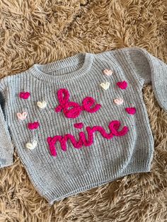 a sweater that says be mine on it sitting on the floor next to a teddy bear