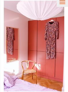 a bedroom with pink walls and wooden flooring, two hanging clothes on the closet doors