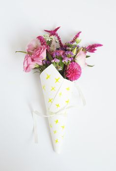 a bouquet of flowers in a paper cone on a white surface with a ribbon tied around it