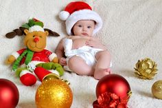 a baby wearing a santa hat sitting next to christmas ornaments and a teddy bear on a blanket