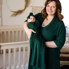 a woman holding a baby in her arms and smiling at the camera while standing next to a crib