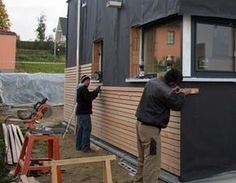 two men are working on the side of a house that's being built with siding