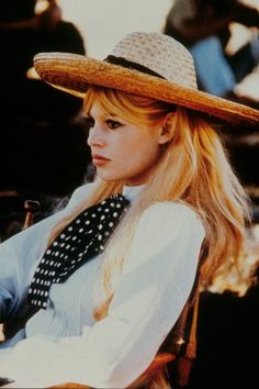 a woman with long blonde hair wearing a hat and sitting in a chair looking to the side