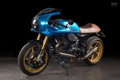 a blue motorcycle parked on top of a cement floor next to a black background with gold rims