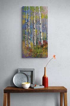 a painting is hanging on the wall above a wooden table with dishes and vases