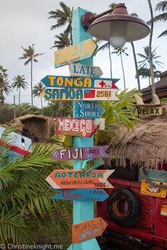 a pole with many signs on it in front of some palm trees and a building