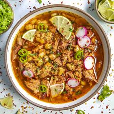 a bowl filled with meat and vegetables on top of a white table next to limes