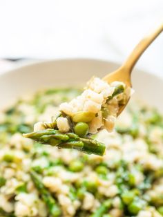 a spoon full of rice and asparagus in a white bowl with a wooden spoon