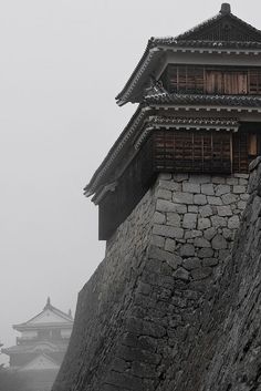 an old building on top of a rock wall in the middle of a foggy day