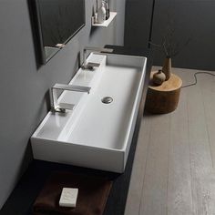 a bathroom sink sitting on top of a wooden floor next to a mirror and vase