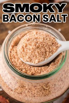 a glass jar filled with bacon salt on top of a wooden table next to a spoon