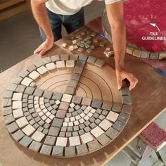 a man is making a mosaic tile design on a table with his hands and feet