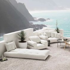 an outdoor seating area overlooking the ocean with white couches and plants on top of it