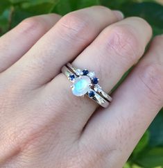 a woman's hand wearing a ring with an opal and blue sapphire stones