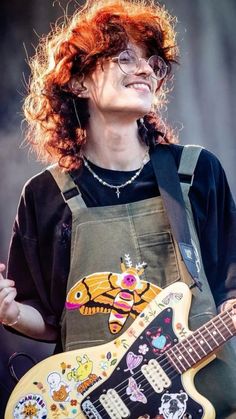 a woman with red hair and glasses playing an electric guitar on stage at a music festival