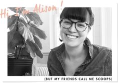 a black and white photo of a woman with glasses smiling at the camera, next to a potted plant