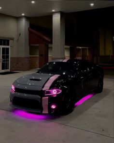 a black and pink sports car parked in front of a building with lights on it