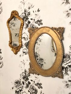 there is a mirror on the wall next to a flowered wall paper with a gold frame