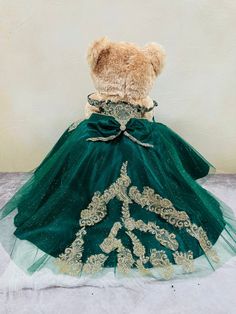 a teddy bear dressed in a green dress with gold trimmings on the skirt