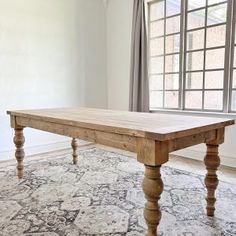 a large wooden table sitting on top of a rug in a living room next to a window