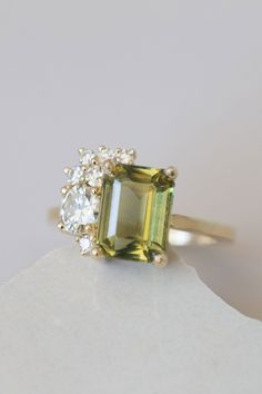 an emerald and diamond ring sitting on top of a white piece of paper