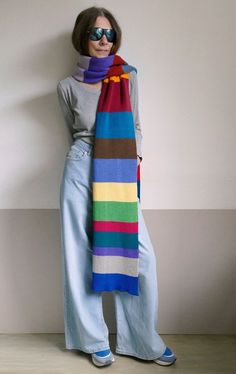 a woman is standing in front of a wall with a colorful scarf on her neck