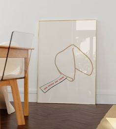 a white framed art print sitting on top of a hard wood floor next to a chair