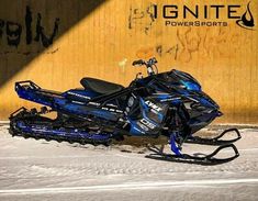 a blue and black snowmobile parked in front of a wall with graffiti on it