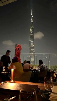 people are sitting at tables in front of the burj dubai tower, which is lit up