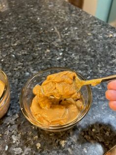 a person holding a spoon full of peanut butter in front of another bowl filled with peanut butter