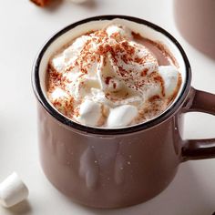 hot chocolate with marshmallows and whipped cream in a brown mug on a white table