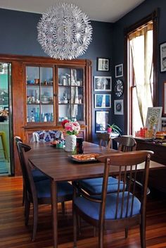 a dinning room table with blue chairs and pictures on the wall in the background