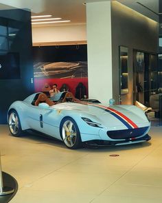 a blue sports car parked inside of a building next to a man sitting in the driver's seat