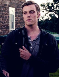 a young man standing in front of a brick building with his hands crossed and looking at the camera