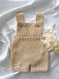 a crocheted baby's overalls and a dried flower on a white sheet