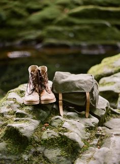 a pair of shoes sitting on top of a moss covered rock next to a bag