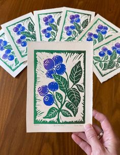 four blue flowers are shown in green and purple on white cards, with one being held up to the camera