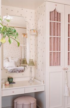 a white dressing table with a mirror, stool and flower pot on top of it