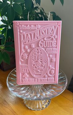 a pink book sitting on top of a glass plate next to a potted plant