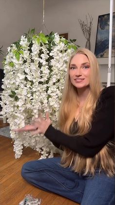 a woman sitting on the floor in front of a vase with white flowers behind her