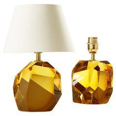 an orange glass table lamp with a white shade on the top and one yellow glass vase next to it