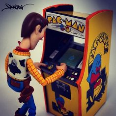 a toy figurine standing next to an old fashioned game machine that says pac - man