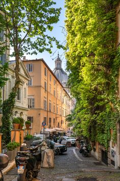 an alleyway with parked cars and motorcycles on the side walk in front of tall buildings