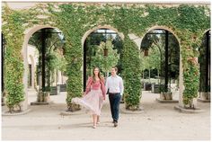 a man and woman walking through an archway covered in green ivy, with one holding the other's hand