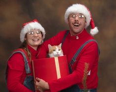 a man and woman in christmas hats holding a present box with a cat on it