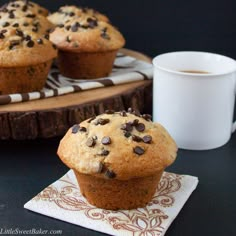 chocolate chip muffins sitting on a napkin next to a cup of coffee and a wooden tray