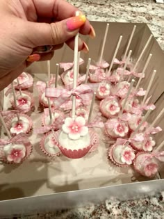 a person is holding up some cupcakes with pink flowers on them