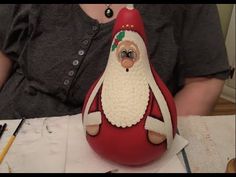 a woman sitting at a table in front of a red vase with a santa clause on it